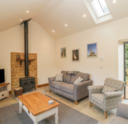 A living room with a sofa armchair coffee table wood stove TV and sliding door to balcony at The Milking Barn in Yeovil Somerset