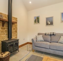 A living room with a wood burning stove couch and framed pictures on the wall at The Milking Barn in Yeovil Somerset