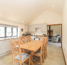 A kitchen with wooden dining table and six chairs next to cabinets and a window at The Milking Barn in Yeovil Somerset