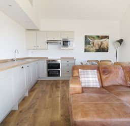A kitchen with white cabinets and wooden countertop next to a brown leather sofa and dining table with chairs at Heron Lodge Castle Farm Wedmore