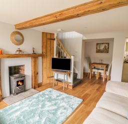 A living room with a wood-burning stove a television on a stand and a dining table at 2 Hillside Cottages in Felixstowe Suffolk