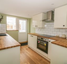 A kitchen with wood countertops white cabinets an electric stove a toaster a microwave and a door with a window at 2 Hillside Cottages in Felixstowe Suffolk