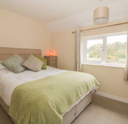 A bedroom with a bed with green throw and pillows and a window with curtains at 2 Hillside Cottages in Felixstowe Suffolk