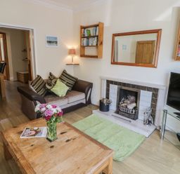 A living room with a sofa table with flowers and a fireplace with a television at Chwech in Menai Bridge