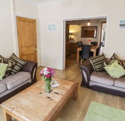 A living room with two sofas a wooden coffee table with flowers and a view into a dining area at Chwech in Menai Bridge