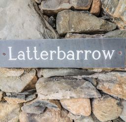 A rectangular sign with the word Latterbarrow mounted on a stone wall at Latterbarrow in Hawkshead
