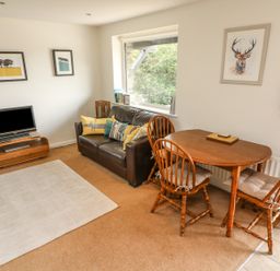 A living room with a leather sofa a wooden dining table with three chairs a television on a wooden stand and framed pictures on the walls at Latterbarrow in Hawkshead