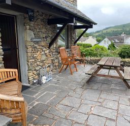 A stone patio with wooden chairs a picnic table and potted plants outside a stone building at Latterbarrow in Hawkshead