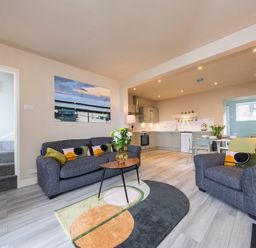 An open plan living room and kitchen with sofas a round table and a colorful rug at Harbour View Cottage in Watchet