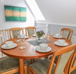 A dining room with a wooden table set for six with white dishes and glasses and a vase with flowers on the table at Running Waters in Callington