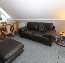 A living room with a brown leather sofa and ottoman a wooden dining table with chairs and a lamp on a side table at Running Waters in Callington
