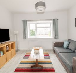 A living room with a sofa a wooden coffee table a striped rug a wooden cabinet with a TV and a window at Swanage Bay Apartment in Swanage