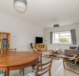 A living room with a wooden dining table and chairs a bookshelf a sofa an armchair a coffee table a TV and a window with curtains at Swanage Bay Apartment in Swanage