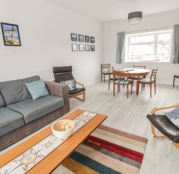A living room with a gray sofa a wooden coffee table a black armchair with a pillow and a round dining table with chairs at Swanage Bay Apartment in Swanage