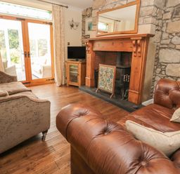 A living room with a stone fireplace a leather sofa fabric sofa wooden floor and glass doors at Red Squirrel Cottage 5 Biddlestone in Rothbury