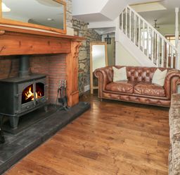 A living room with a wood burning stove fireplace leather sofa and staircase at Red Squirrel Cottage 5 Biddlestone Rothbury