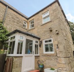 The exterior of a stone house with white framed windows and a white door with glass panels at Red Squirrel Cottage 5 Biddlestone in Rothbury