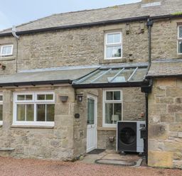 The exterior of a stone house with multiple windows a white door a glass porch roof and an outdoor air conditioning unit at Red Squirrel Cottage 5 Biddlestone in Rothbury