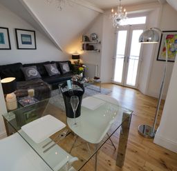 A living room with a glass dining table a black leather sofa and double doors at Flat 3 Peacehaven Sandsend near Whitby