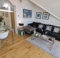 A living room with a black sofa a glass coffee table and a glass dining table at Flat 3 Peacehaven Sandsend near Whitby