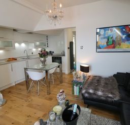 A kitchen and living area with white cabinets glass table and chairs a black sofa with a fur throw at Flat 3 Peacehaven Sandsend near Whitby