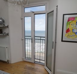 A room with wooden floor an open glass door overlooking the sea a bookshelf and framed artwork on the wall at Flat 3 Peacehaven Sandsend near Whitby