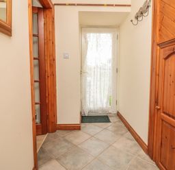 A hallway with tiled floor wooden doors and a door with a lace curtain at Sorrel Cottage in Padstow