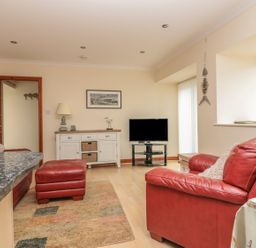 A living room with red leather sofas a television on a stand a white sideboard with a lamp and decorations at Sorrel Cottage in Padstow
