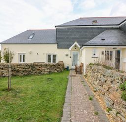 A house with beige walls a slate roof a stone wall and a grass lawn at Sorrel Cottage in Padstow