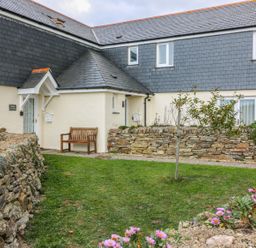 A stone wall garden with a wooden bench and a small tree outside a cottage with slate roofing at Sorrel Cottage in Padstow
