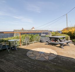 A wooden outdoor deck with chairs a round table picnic bench and plants at Blackbrae Cabin in Glenboig near Coatbridge Glasgow and Stirling