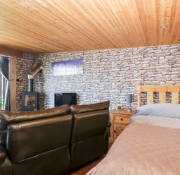 A bedroom with a bed a wooden nightstand a black leather sofa a wood stove and stone patterned wallpaper at Blackbrae Cabin in Glenboig near Coatbridge Glasgow and Stirling