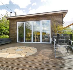 A wooden deck with a circular stone pattern in front of a cabin with glass doors and metal chairs at Blackbrae Cabin in Glenboig near Coatbridge Glasgow and Stirling