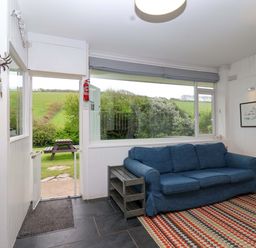 A snug with a sofa and door leading outside at 2 Brook Cottages in Hope Cove