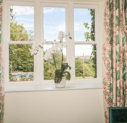A window with a white orchid on the sill and patterned curtains a green chair with a red cushion at Newbiggin Cottage in Blanchland