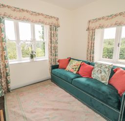 A sitting room with green sofa and floral cushions by two windows with floral curtains at Newbiggin Cottage in Blanchland