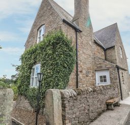 A stone cottage with ivy on the wall and a stone fence along a road at Newbiggin Cottage in Blanchland