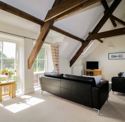 A living room with black leather sofas wooden beams and windows with curtains at Carpenters Cottage in Cockermouth