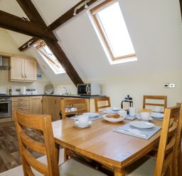 A dining table set for tea in a kitchen with wooden beams and skylight windows at Carpenters Cottage in Cockermouth