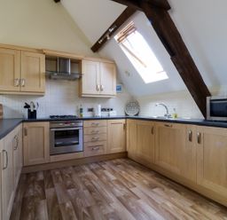 A kitchen with wooden cabinets a stove a microwave and a skylight window at Carpenters Cottage in Cockermouth