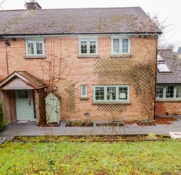 The back of a brick house with green framed windows a small covered porch and a garden with a grassy lawn at Hiraeth Cwmtaf near Cefn-Coed-Y-Cymmer