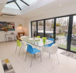 A dining area with a glass table and colorful chairs next to large sliding glass doors opening to a garden at Hiraeth in Cwmtaf near Cefn-Coed-Y-Cymmer