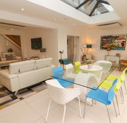 A dining area with colorful chairs and a glass table next to a living room with sofas and a television at Hiraeth in Cwmtaf near Cefn-Coed-Y-Cymmer