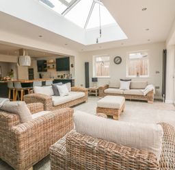 A sitting area with wicker sofas and cushions under a skylight near a kitchen and dining area at The Orchard in Crantock