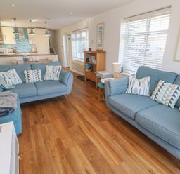 A living room with blue sofas and cushions next to a kitchen with a dining table at Kittiwake in Crantock