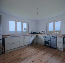 A kitchen with cabinets a refrigerator dishwasher stove sink and two windows at Kareena in Crantock