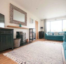 A living room with teal sofas a large window and a rug at Keelyn in Crantock