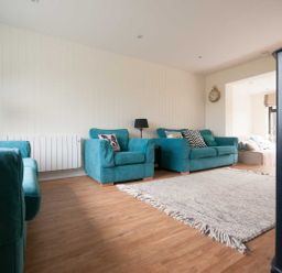 A living room with teal armchairs and sofa a floor lamp a wall clock and a light rug on wooden floor at Keelyn in Crantock