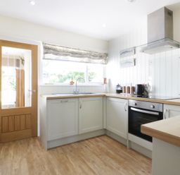 A kitchen with wooden countertops a stainless steel oven a window with a patterned blind and a wooden door at Keelyn in Crantock