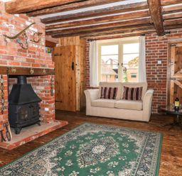 A living room with a brick fireplace wood stove beige sofa with striped cushions and wooden doors at Downs View Dairy in West Tytherley